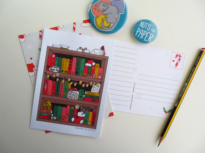 Cartão postal ilustrado com estante de livros e decoração de Natal, pins redondos azuis, lápis e envelope com padrão de bengalas vermelhas