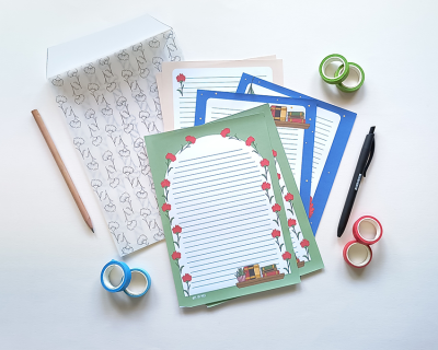 Papel de carta com decoração de livros e rosas, lápis, caneta, fita adesiva colorida e envelope com padrão de gatos
