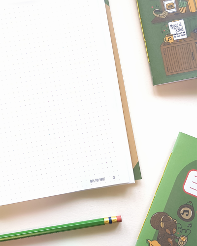 Página de caderno pontilhada, lápis verde e capa de caderno verde com ilustração musical