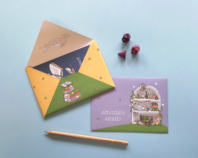 Envelope colorido, cartão lilás com texto e desenhos, três dados de jogos e lápis laranja sobre fundo azul claro