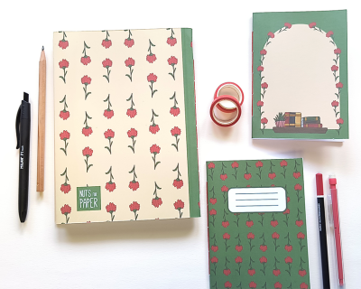 Dois cadernos e um bloco com padrão de flores, rolos de fita adesiva e canetas