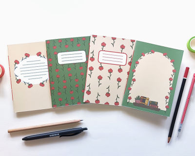 Quatro cadernos de capas florais com áreas para escrever, rodeados por canetas e lápis