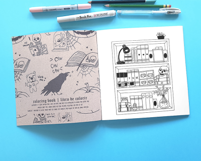 Livro de colorir aberto com ilustrações e canetas ao fundo