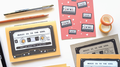 Cadernos com ilustração de fitas cassete e texto sobre a música, lápis, pincel, folha decorativa e fitas adesivas