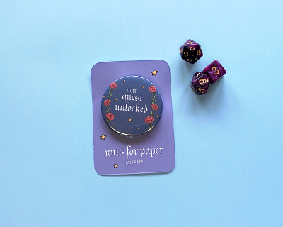 Chapa decorativa com texto 'quest unlocked' e dois dados de jogo em fundo azul