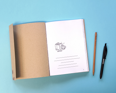 Caderno aberto com desenho de pacote de leite e chávena, lápis e caneta sobre fundo azul.