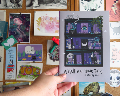 Revista Witching Hour Tales com capa lilás e ilustrações de gatos e livros, à frente de mural com várias ilustrações.