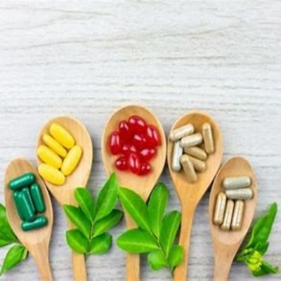 Cinco colheres de madeira com cápsulas coloridas e folhas verdes sobre uma mesa clara