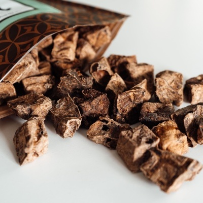 Pedaços de alimento seco castanho e bege espalhados ao lado de embalagem aberta