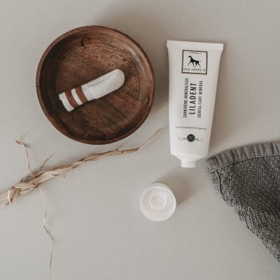 Tubo de creme branco aberto, prato de madeira com objeto branco e castanho, rede cinza e ramos secos