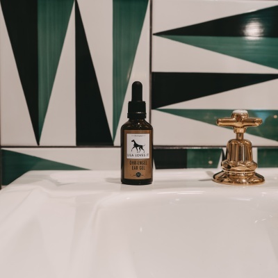 Frasco de gel para orelhas em pia branca com torneira dourada e azulejos geométricos verdes