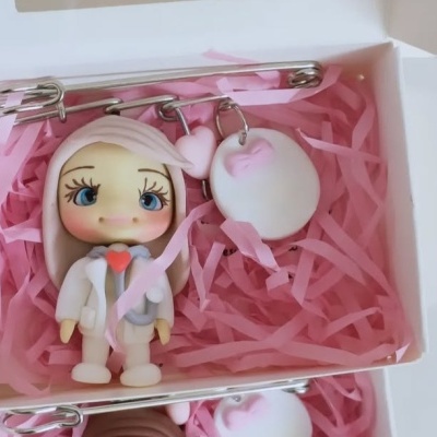 Broche com pendente de boneco em caixa branca com enchimento rosa