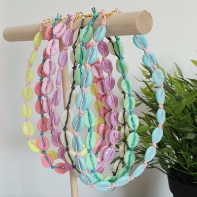 Colares de contas coloridas pendurados em suporte de madeira junto a planta verde