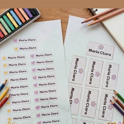Etiquetas adesivas personalizadas com nome e desenhos coloridos, lápis de cor e giz pastel sobre superfície de madeira