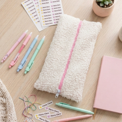 Estojo pelúcia branco com fecho cor-de-rosa e canetas pastel numa mesa de madeira