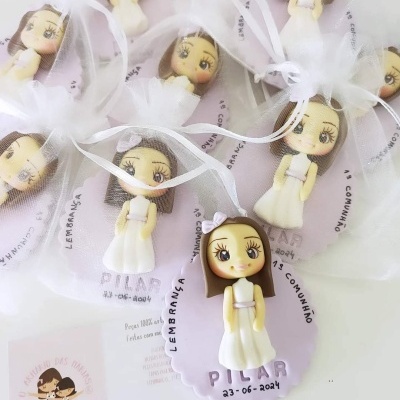 Lembranças da primeira comunhão com menina em vestido branco sobre etiquetas roxas e embaladas em bolsas de tule branco.