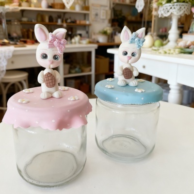 Dois frascos com tampas decoradas com coelhos de pasta polimérica em rosa e azul