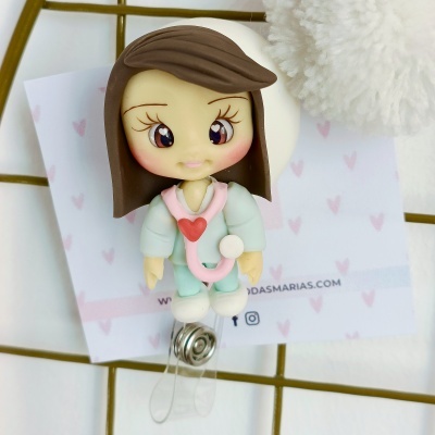 Figura decorativa de médica com bata azul clara, estetoscópio rosa, cabelo castanho e mola metálica