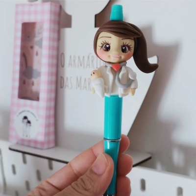 Caneta azul com topo decorado com figura de fada ou boneca segurando amuletos