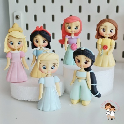 Seis bonecas coloridas em estilo cartoon sobre plataforma branca com painel perfurado ao fundo