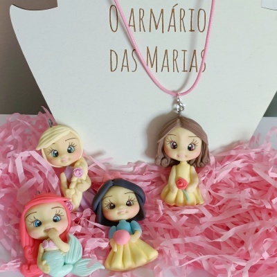 Quatro bonecas coloridas de resina sobre papel rosa com texto ao fundo.