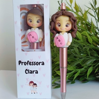 Caneta de cor rosa metálica com tampa em forma de muñeca e caixa branca com texto