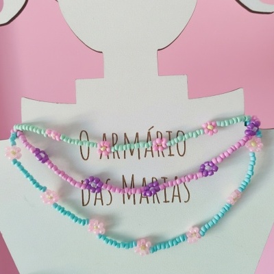 Colares de contas coloridas com pequenas flores em suporte branco e fundo rosa