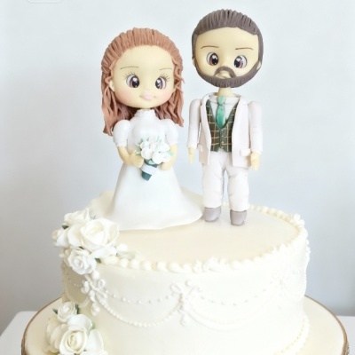 Bolo de casamento branco com figuras de noivos em estilo cartoon no topo