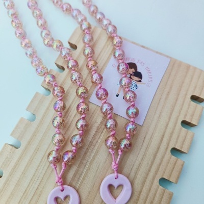 Colares com contas rosa e pendentes em forma de círculo rosa com coração, sobre base de madeira clara