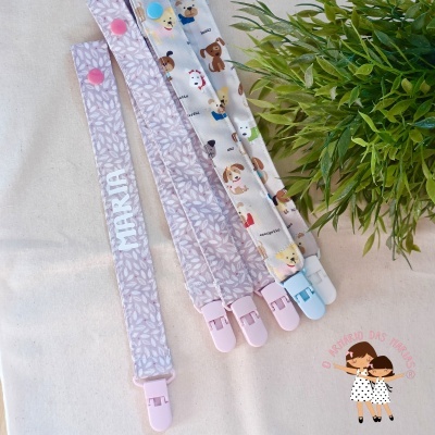 Quatro fitas porta-chupetas com diferentes padrões e presilhas, planta verde ao lado