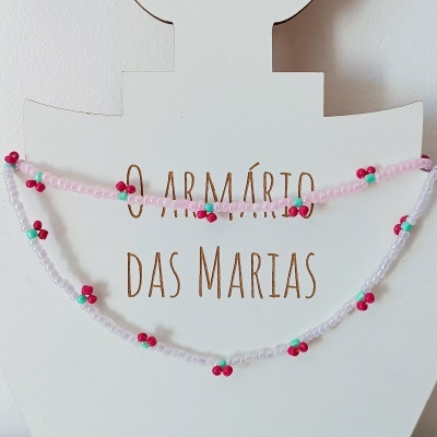 Colar ou pulseira de contas coloridas rosas e brancas com flores vermelhas e verdes sobre suporte branco com o texto O ARMÁRIO DAS MARIAS.