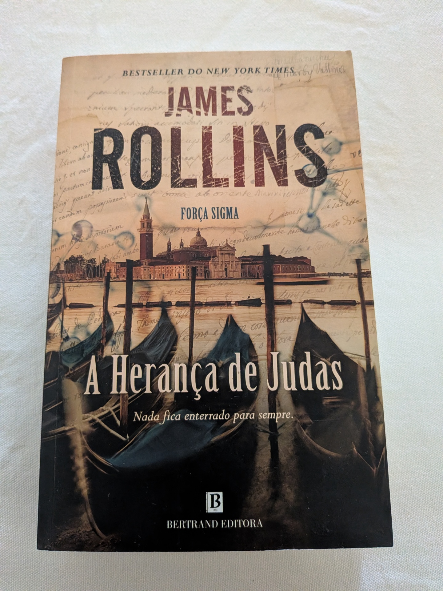 James Rollins - A Herança de Judas Capa de livro A Herança de Judas de James Rollins com imagem de barcos e edifícios históricos.