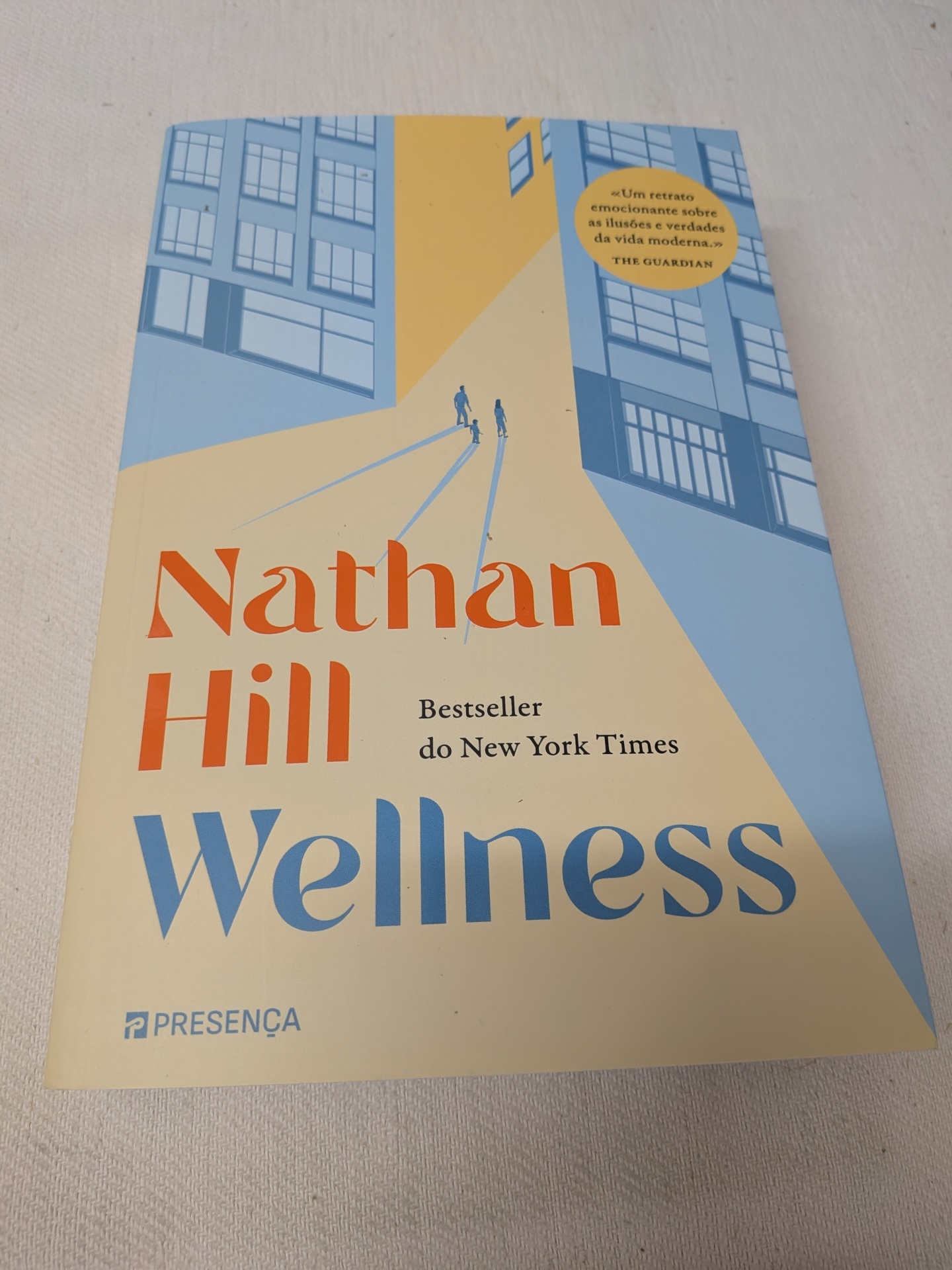 Nathan Hill - Wellness (defeito na capa) Capa de livro com ilustração de prédios e figuras humanas em azul e amarelo