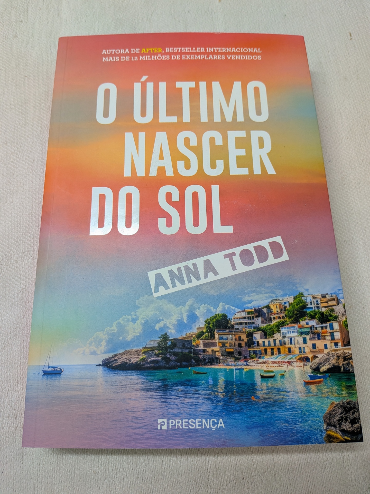 Anna Todd - O Último Nascer do Sol (defeito na capa) Capa do livro O Último Nascer do Sol com vila costeira e pôr do sol colorido