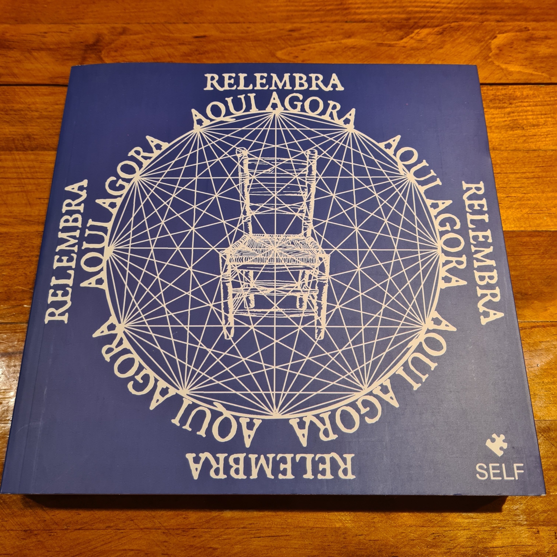 Ram Dass - Aqui Agora Capa azul de livro com cadeira branca e texto circular