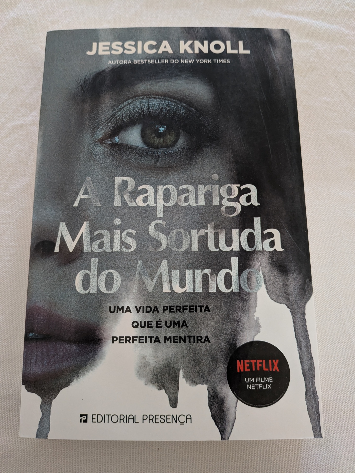 Jessica Knoll - A Rapariga Mais Sortuda do Mundo Capa de livro cinzenta com título e rosto feminino parcial e selo Netflix