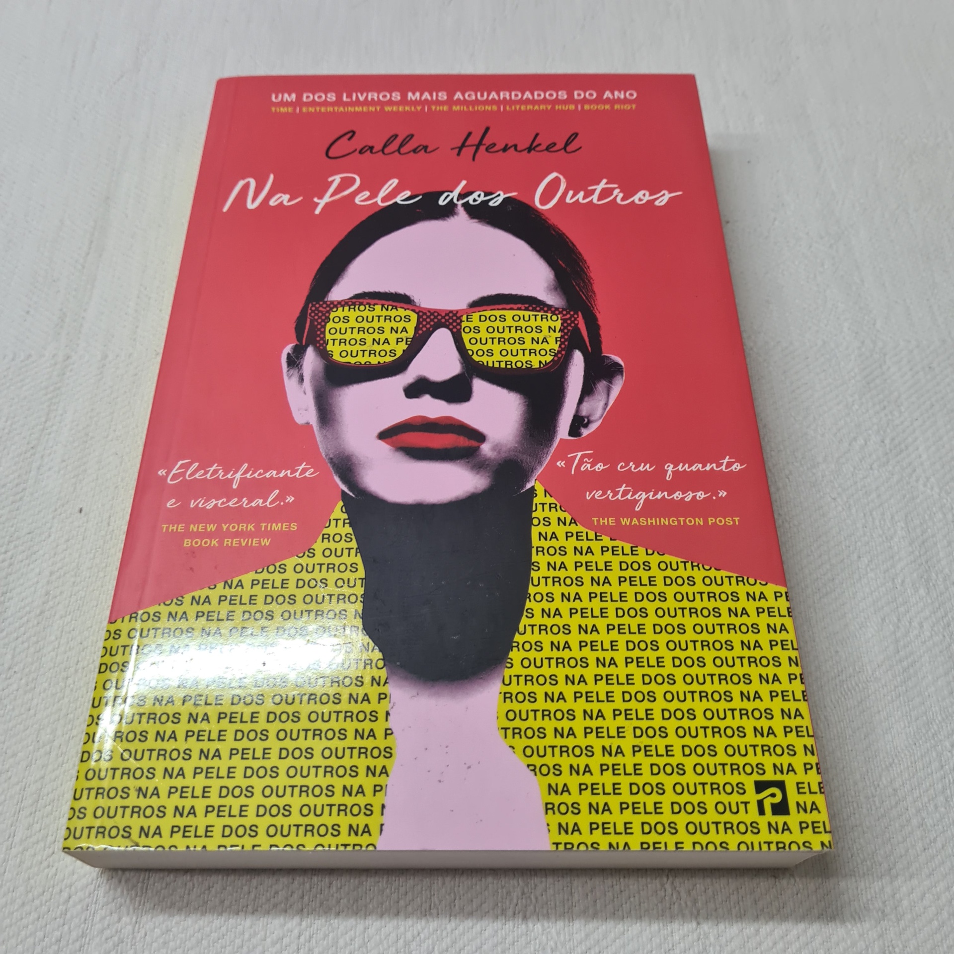 Calla Henkel - Na Pele dos Outros Capa de livro 'Na Pele dos Outros' com ilustração de rosto feminino lilás e óculos amarelos com texto