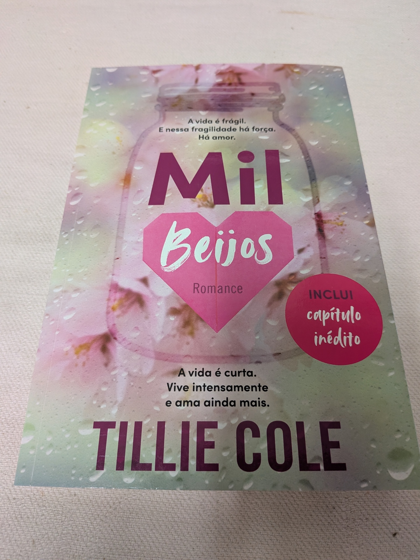 Tillie Cole - Mil Beijos Livro Mil Beijos com capa floral e gotas de água, texto em português e selo rosa de capítulo inédito