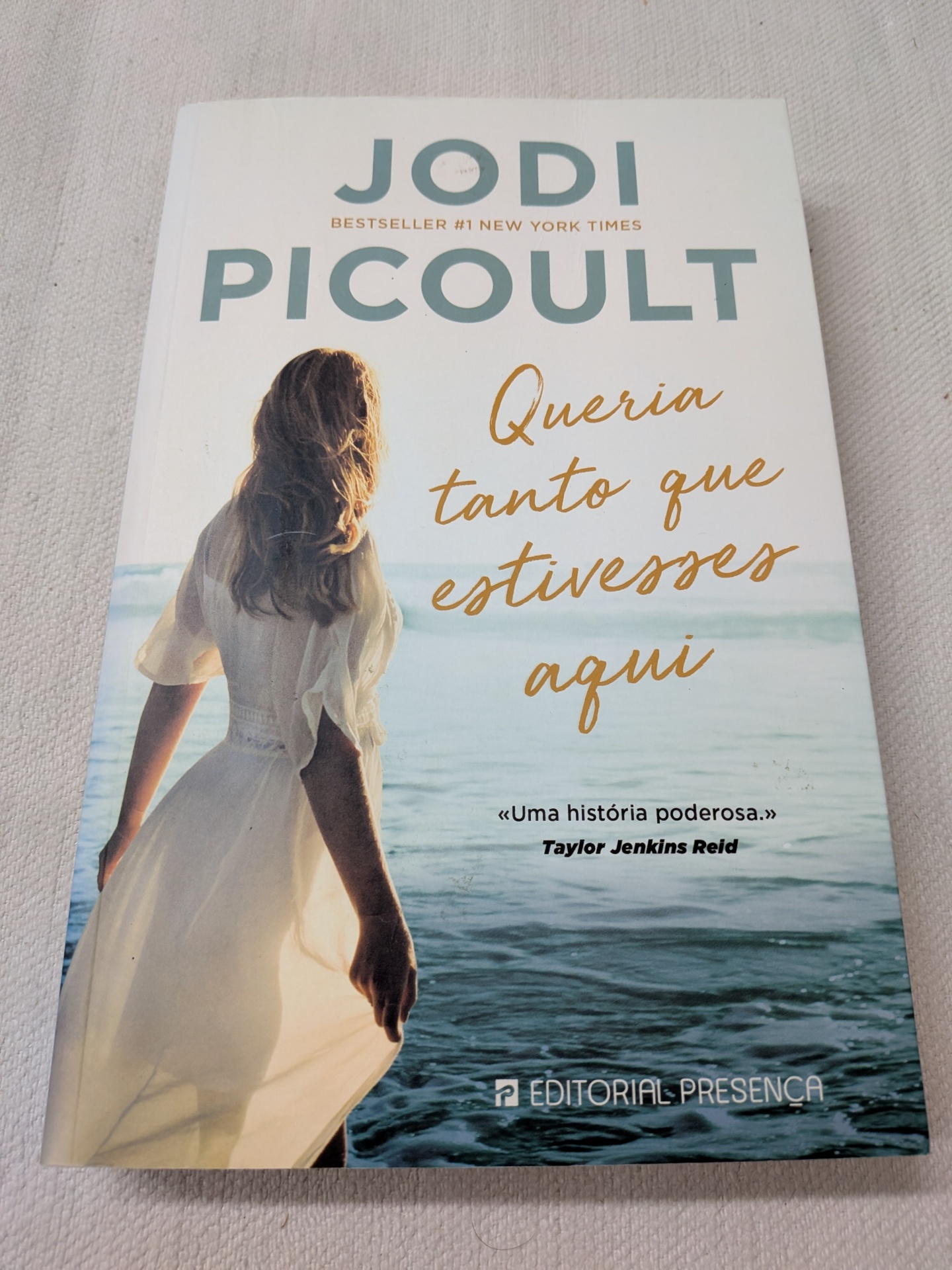 Jodi Picoult - Queria Tanto que Estivesses Aqui Livro Queria tanto que estivesses aqui de Jodi Picoult com imagem de mulher de vestido branco à beira-mar.