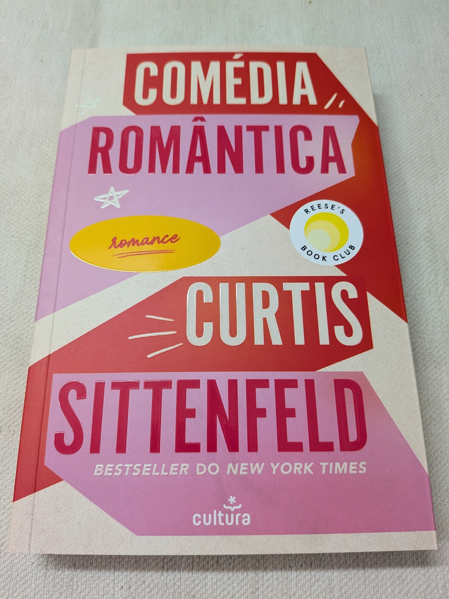 Curtis Sittenfeld - Comédia Romântica Capa de livro em tons vermelhos e rosa com grandes textos e selos.