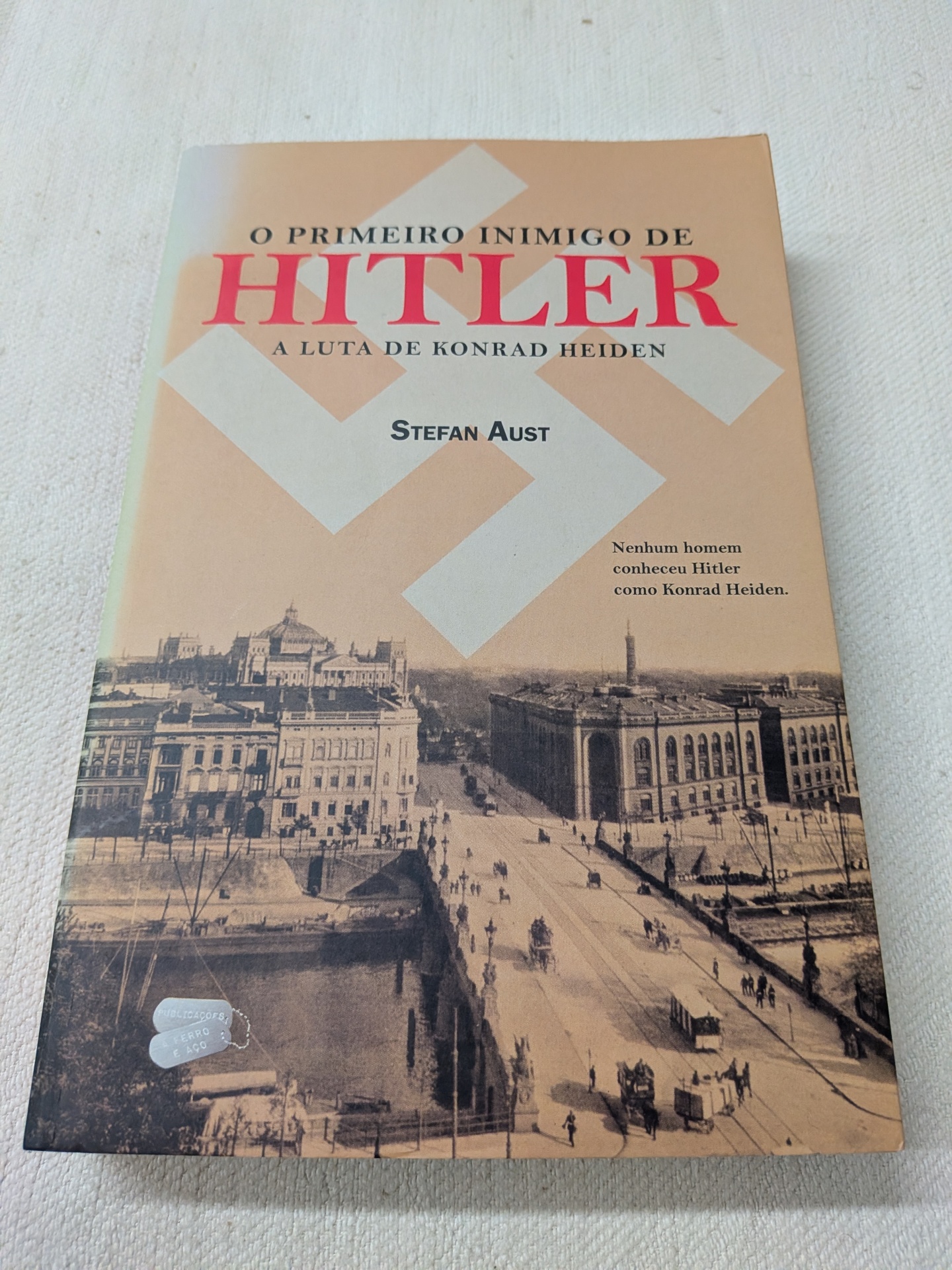 Stefan Aust - O Primeiro Inimigo de Hitler: A Luta De Konrad Heiden Capa de livro em tons bege com título em vermelho e preto e imagem histórica de uma cidade
