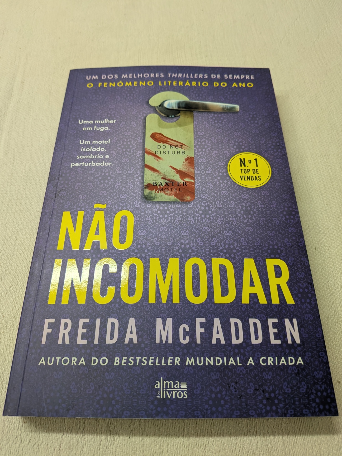 Freida McFadden - Não Incomodar Capa de livro roxa com título NÃO INCOMODAR em amarelo e imagem de pendurador de porta