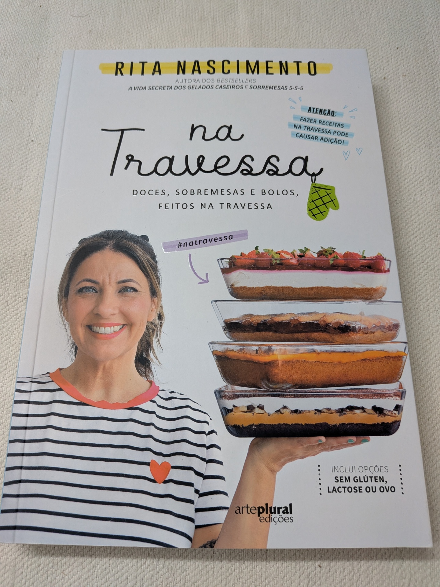 Rita Nascimento - Na Travessa (Doces, sobremesas e bolos, feitos na travessa) Capa de livro Na Travessa com mulher sorridente e travessas de sobremesas empilhadas
