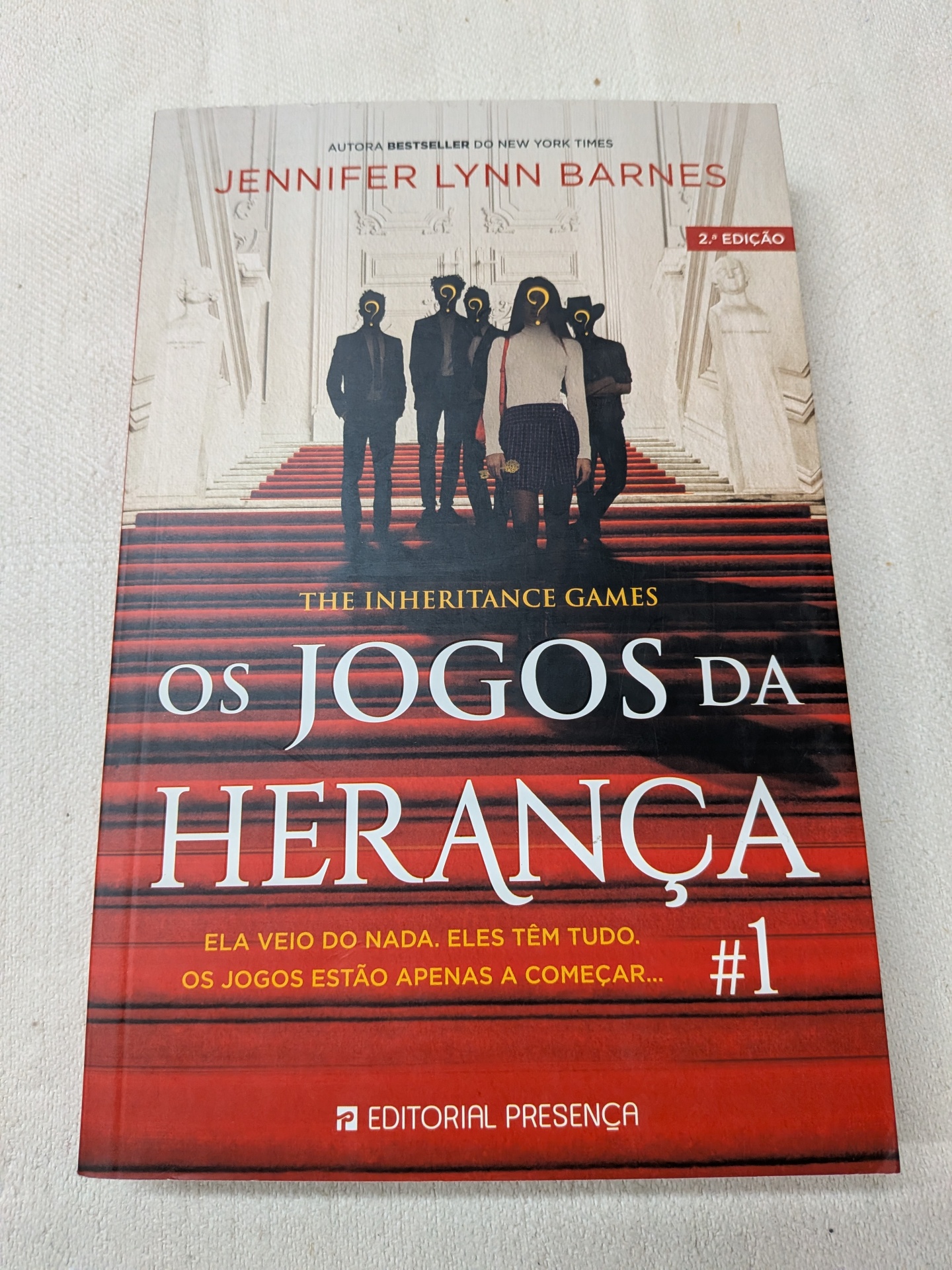 Jennifer Lynn Barnes - Os Jogos da Herança 1 - The Inheritance Games Capa do livro Os Jogos da Herança com escadaria vermelha e figuras humanas.