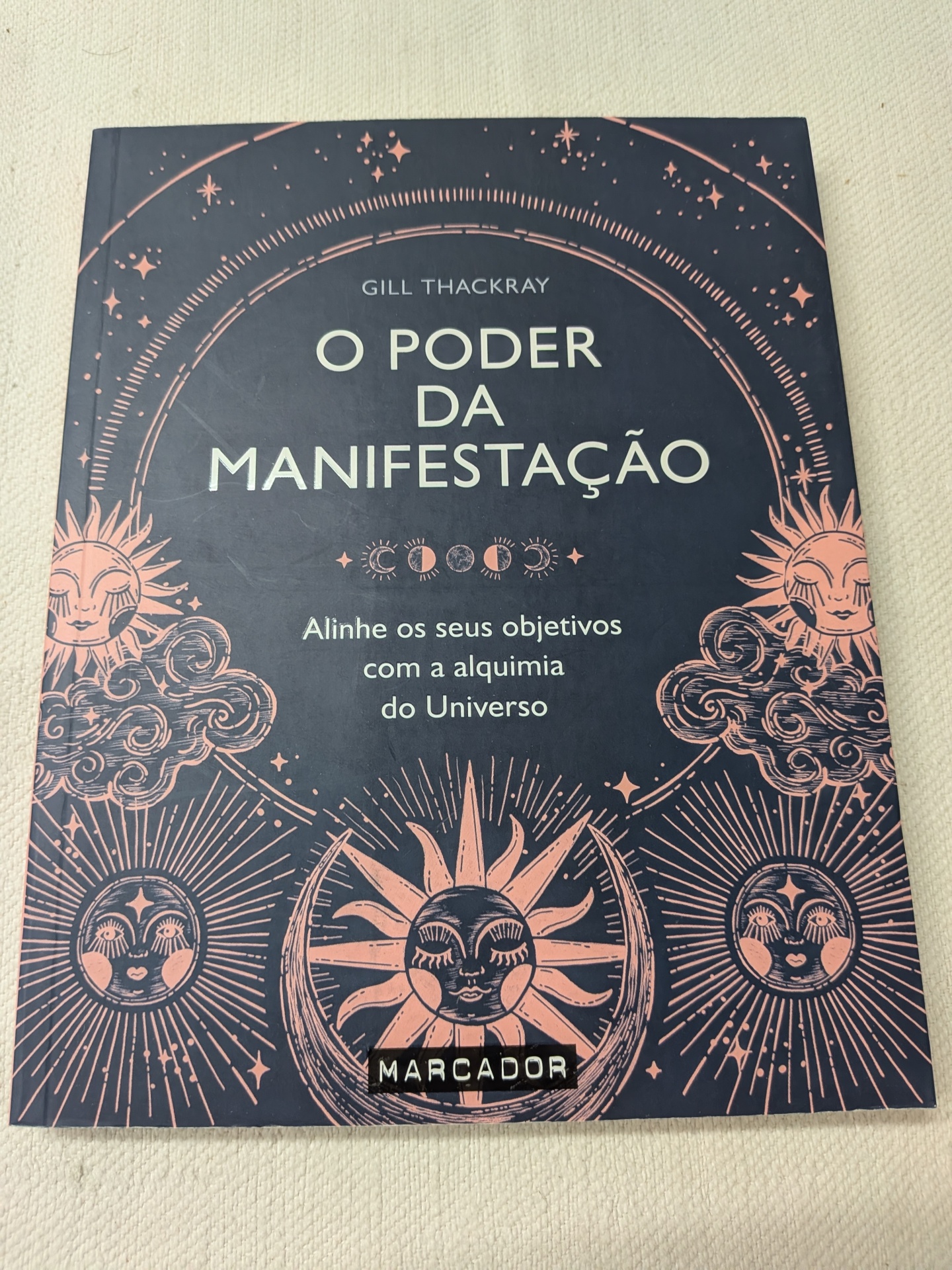 Gill Thackray - O Poder da Manifestação (defeito na capa) Capa de livro azul escura com ilustrações solares e lunares cor rosa e texto título em branco.
