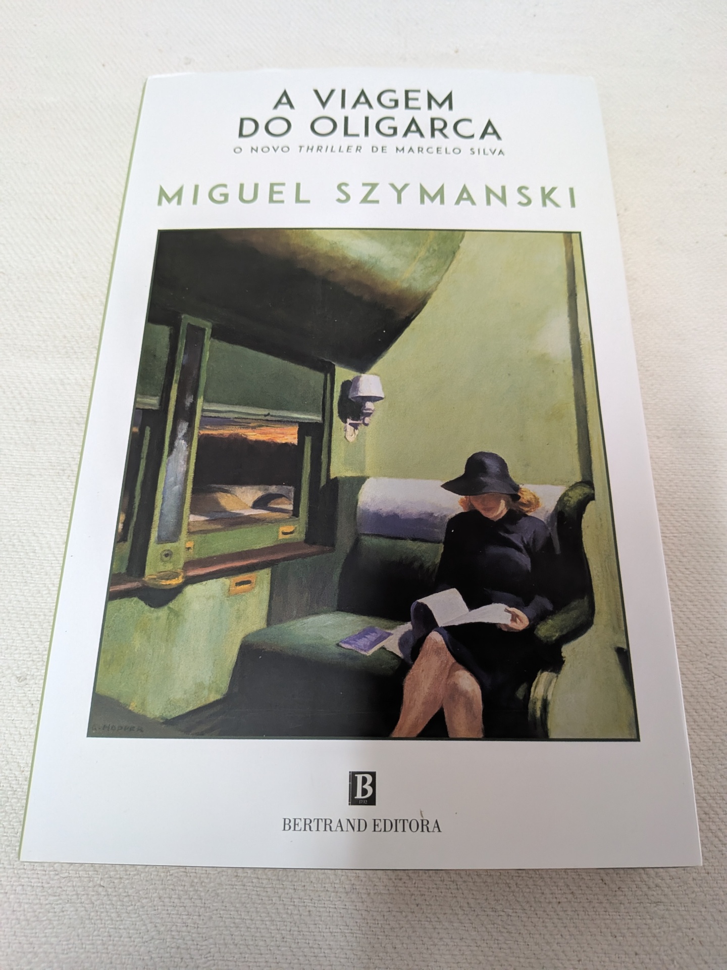 Miguel Szymanski - A Viagem do Oligarca Capa do livro A VIAGEM DO OLIGARCA com ilustração de mulher sentada a ler.