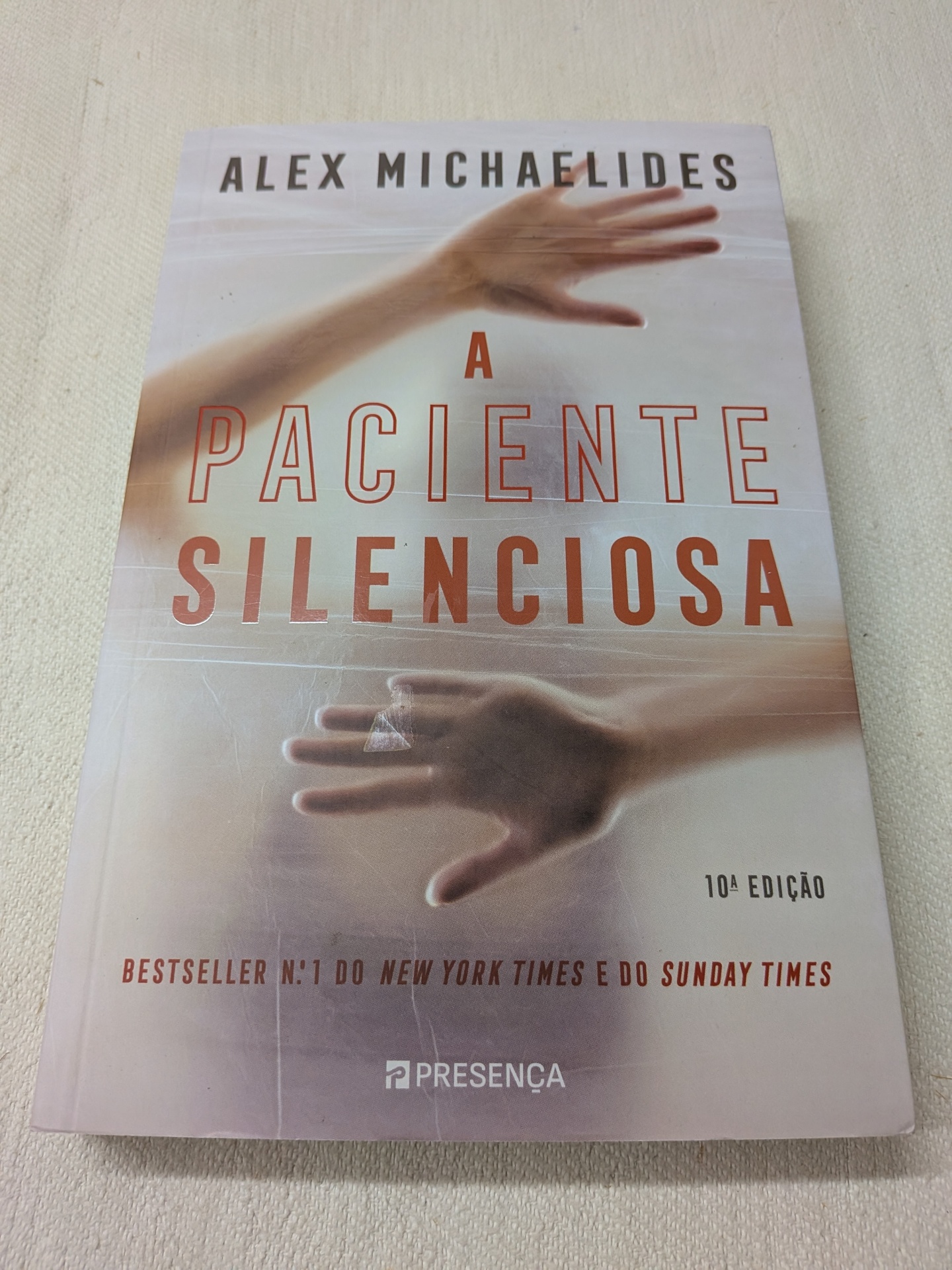 Alex Michaelides - A Paciente Silenciosa Capa do livro A Paciente Silenciosa com texto e imagem de mãos desfocadas