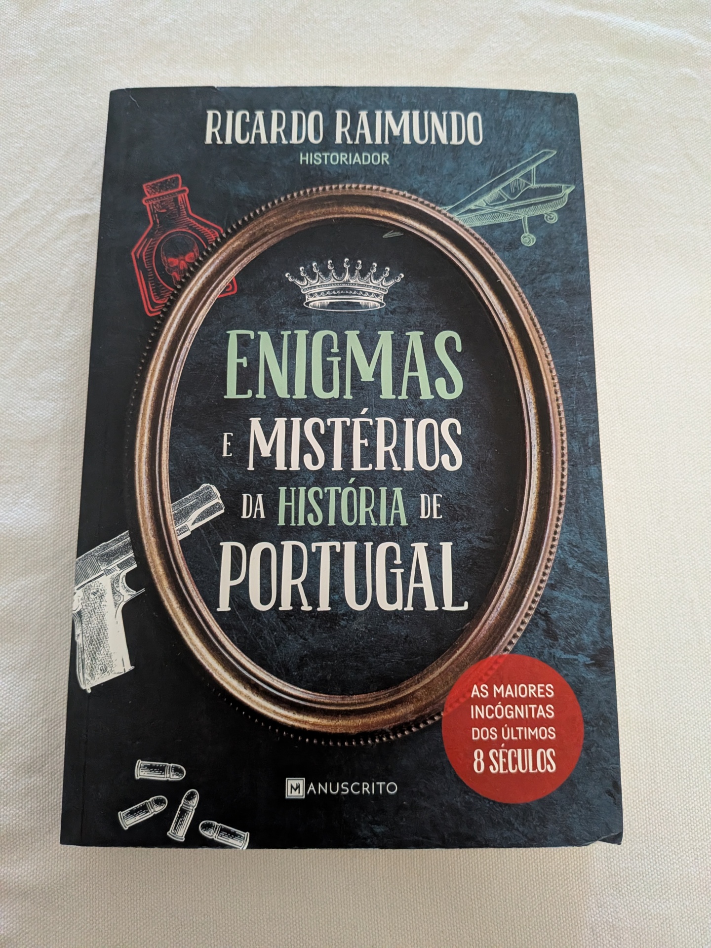 Ricardo Raimundo - Enigmas e Mistérios da História de Portugal Livro Enigmas e Mistérios da História de Portugal com capa preta e moldura castanha oval