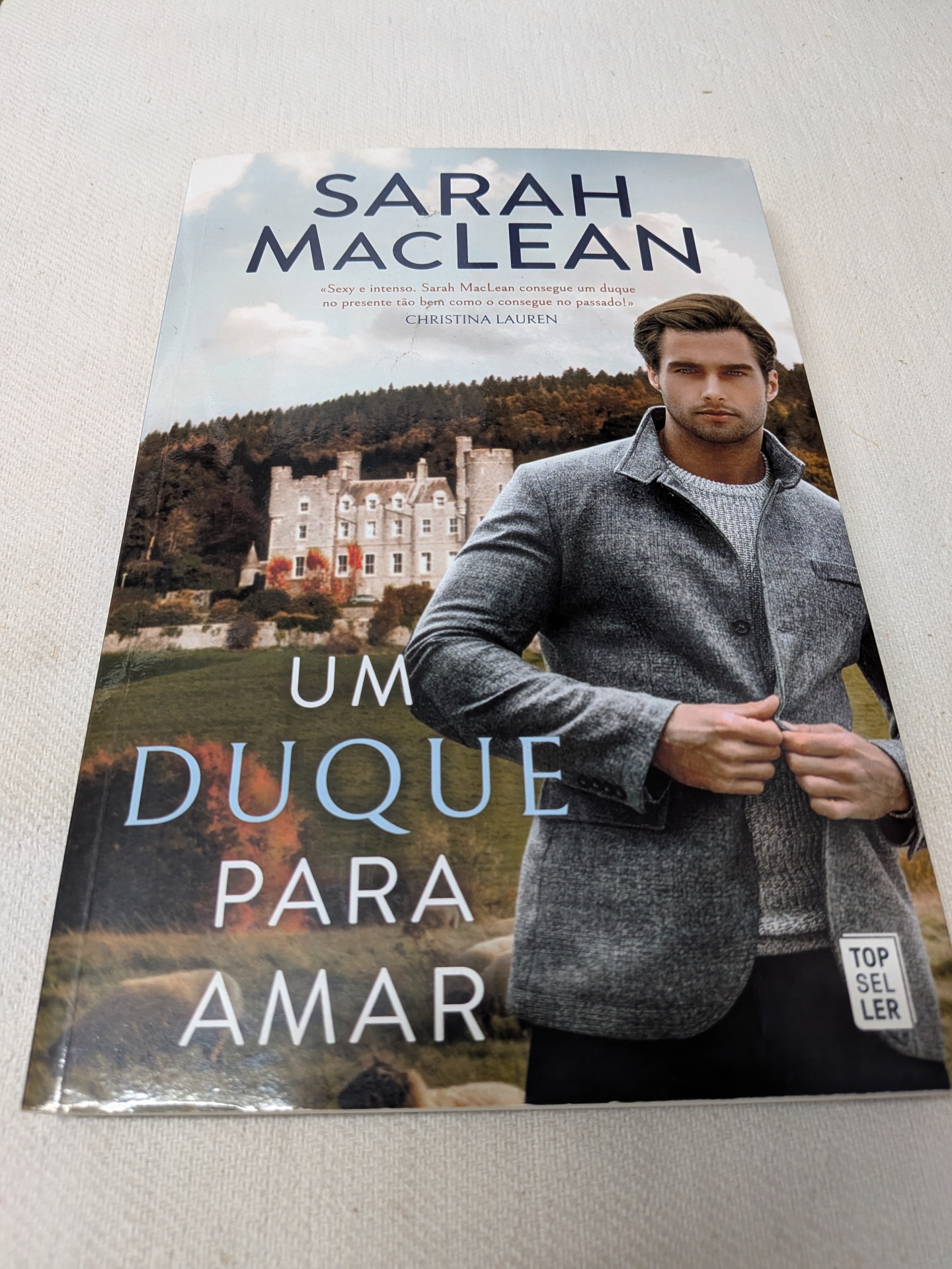Sarah MacLean - Um Duque para Amar Capa de livro com homem de casaco cinza e castelo ao fundo, título UM DUQUE PARA AMAR de Sarah MacLean