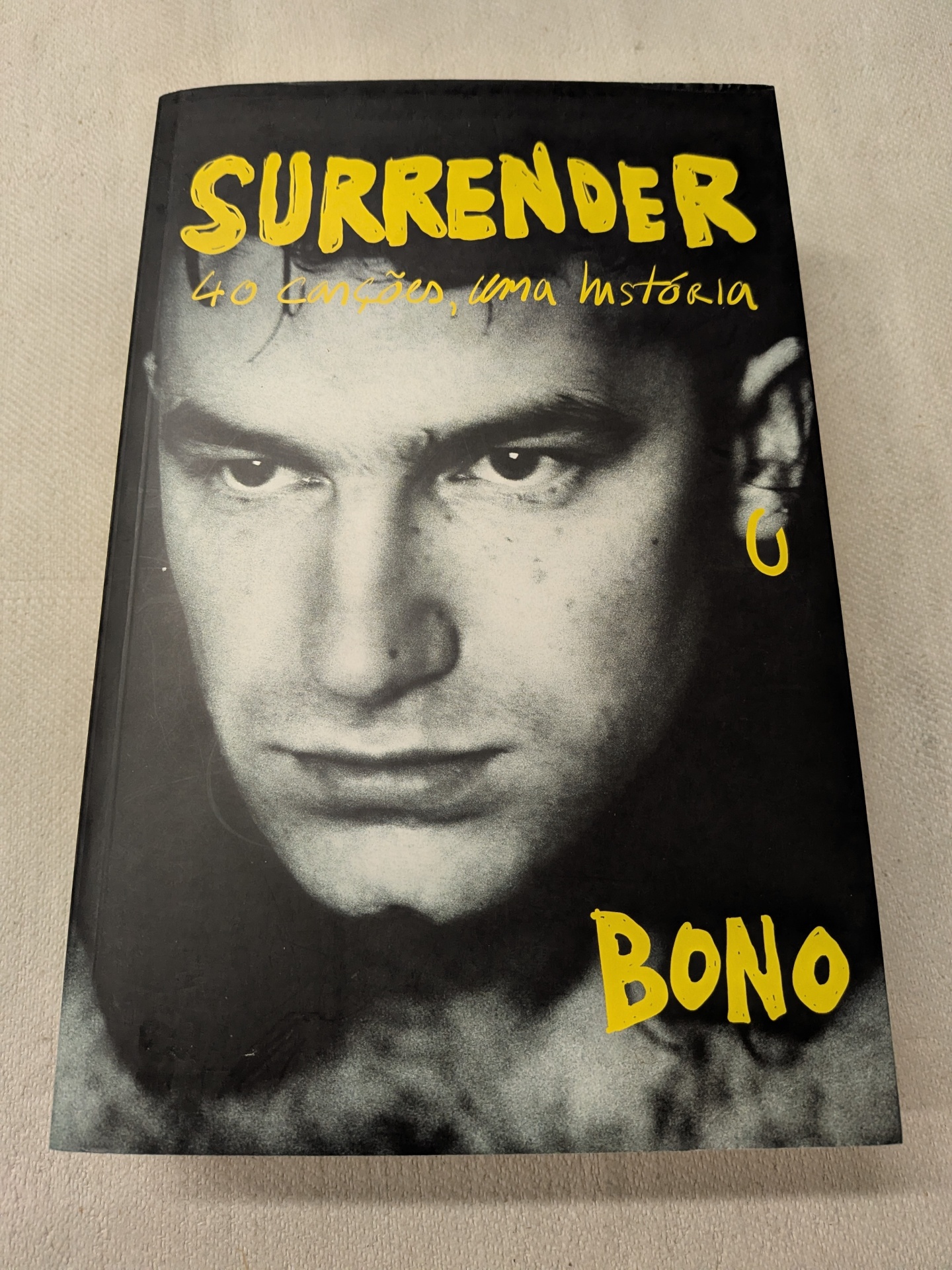Bono - Surrender - 40 canções, uma história Capa de livro mostrando um rosto masculino em preto e branco com texto amarelo.